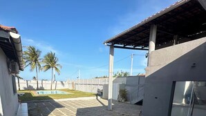 A covered outdoor area with a tiled floor, a pool, and palm trees in the background. - House in Cumbuco  (Caucaia)