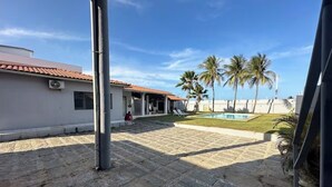 A courtyard with a swimming pool, palm trees, and a building with a tiled roof. - House in Cumbuco  (Caucaia)