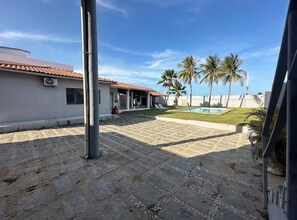 A courtyard with a swimming pool, palm trees, and a building with a tiled roof. - House in Cumbuco  (Caucaia)