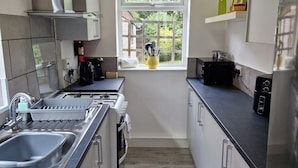 A modern kitchen with a built-in oven, a coffee maker, and a window with a view of greenery. - Spacious 4BR Home w/ Parking – Family-Friendly (Birstall)
