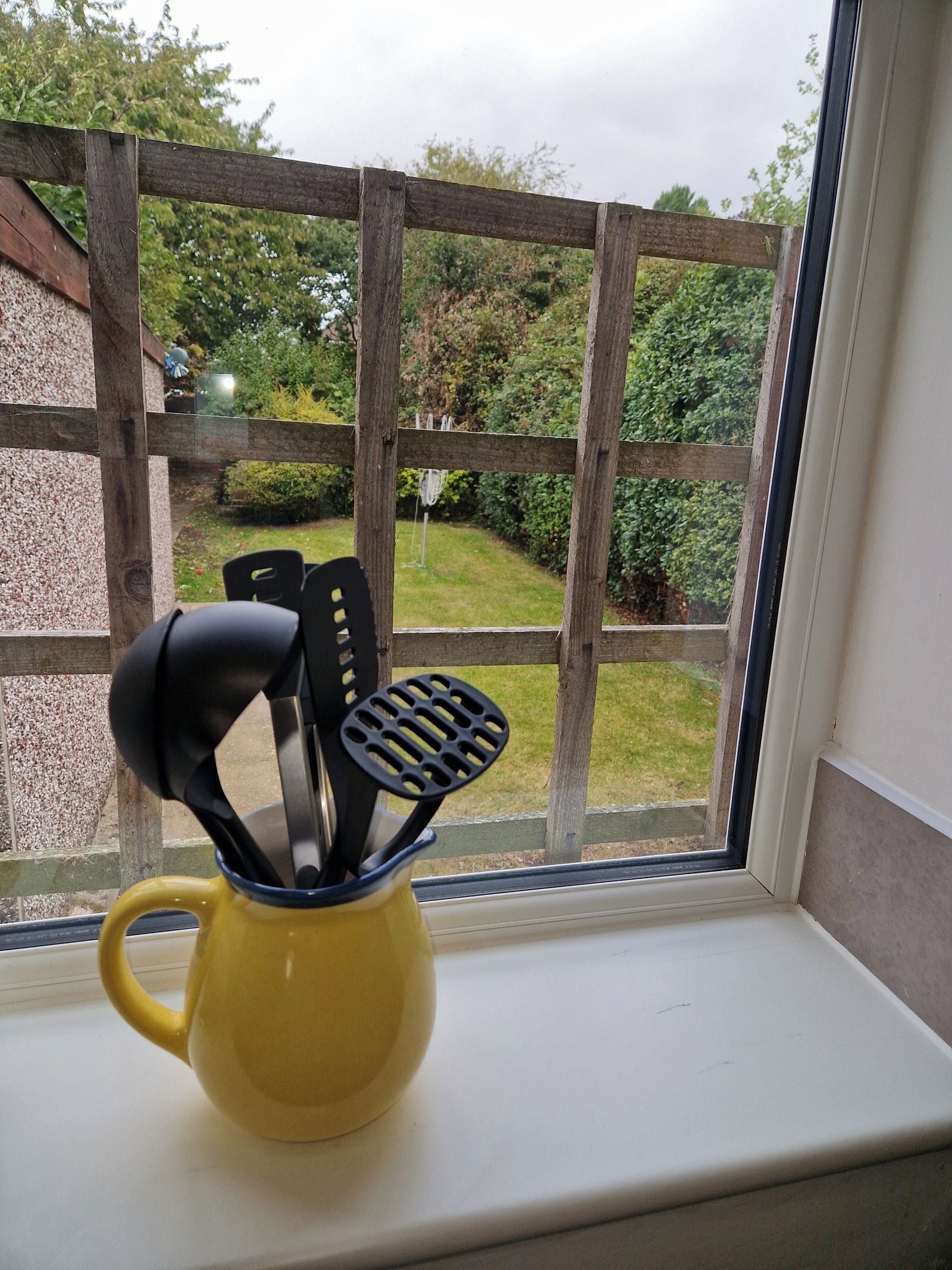 A yellow mug with kitchen utensils on a windowsill.