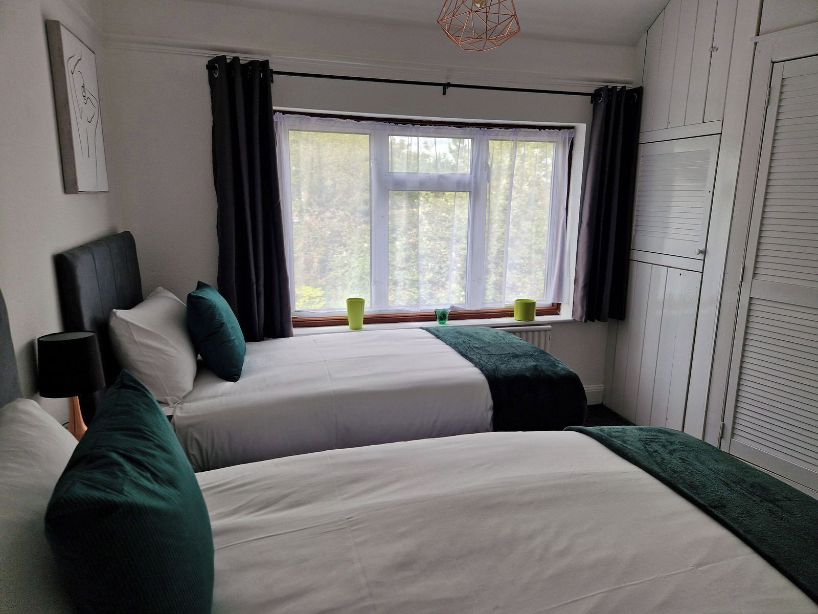 A hotel room with two beds, a window with curtains, a radiator, and a wall-mounted artwork.