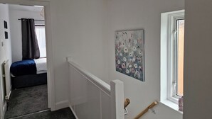 A narrow hallway with a bed in the background, a painting on the wall, and a window with a view. - Spacious 4BR Home w/ Parking – Family-Friendly (Birstall)