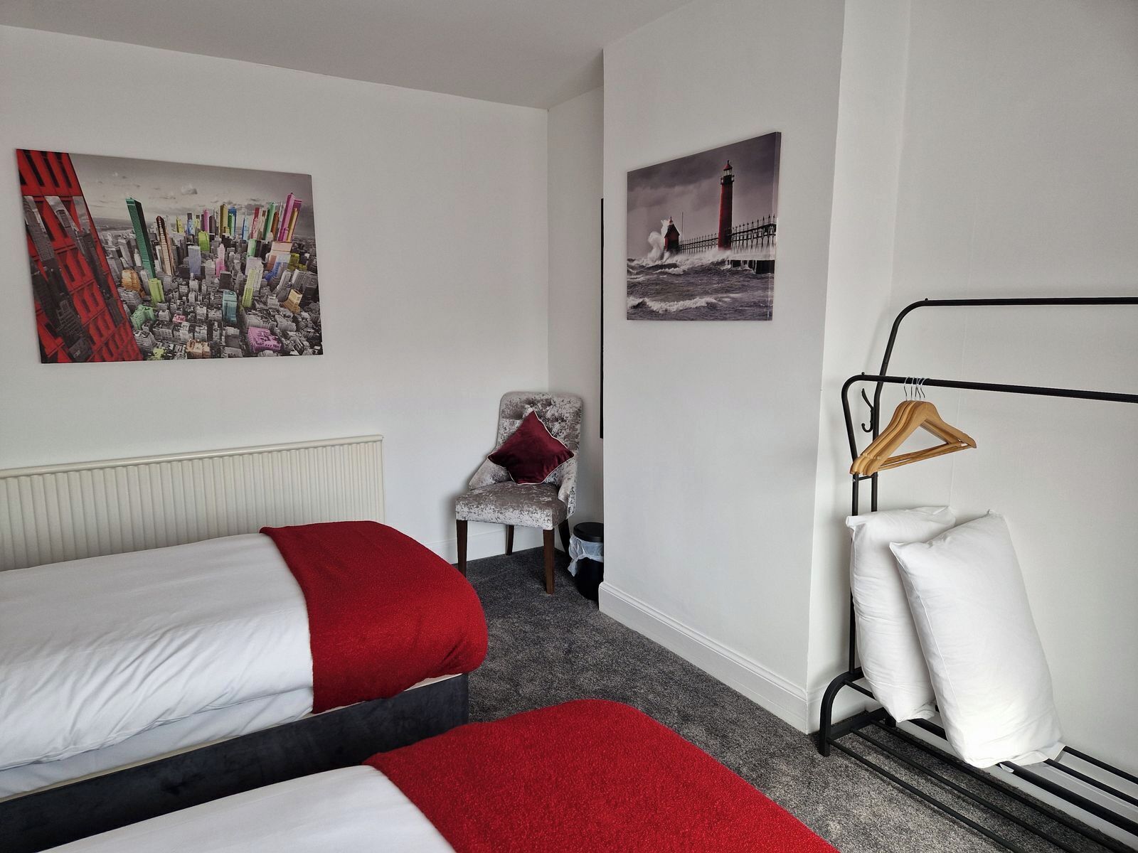A hotel room with two beds, a chair, a radiator, and two wall-mounted pictures.