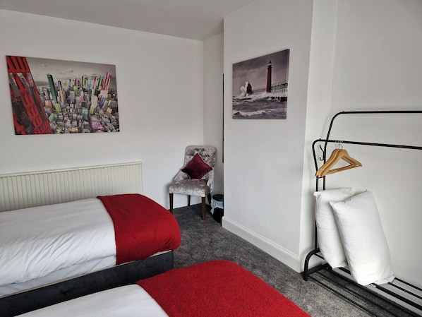 A hotel room with two beds, a chair, a radiator, and two wall-mounted pictures.