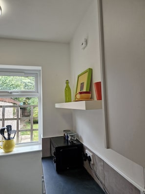 A kitchen with a window, a microwave, and a shelf with kitchenware.
