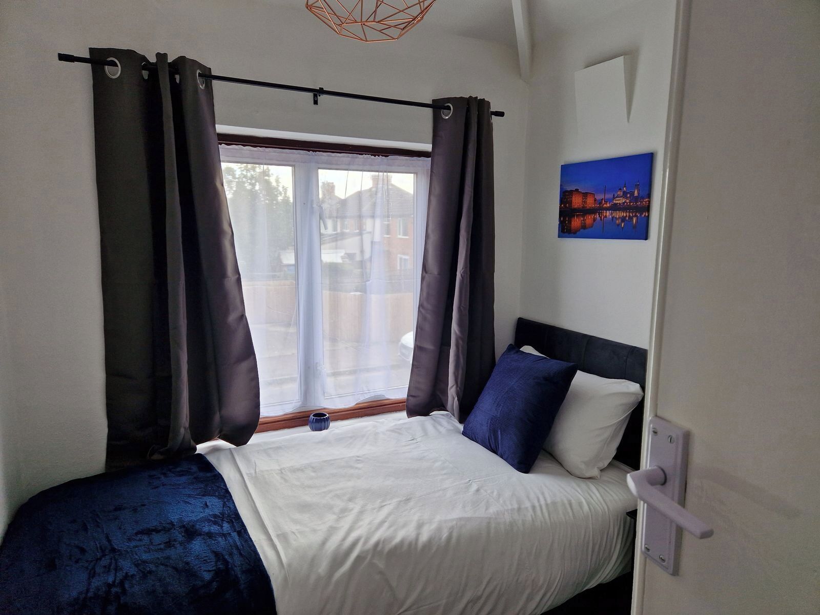 A bedroom with a bed, curtains, a window, and a painting on the wall.