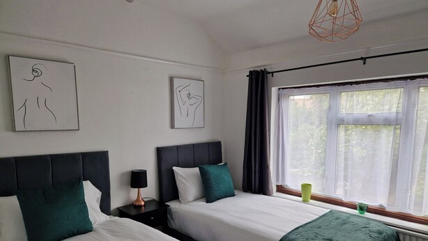 A hotel room with two beds, a nightstand with a lamp, and artwork on the walls. - Spacious 4BR Home w/ Parking – Family-Friendly (Birstall)