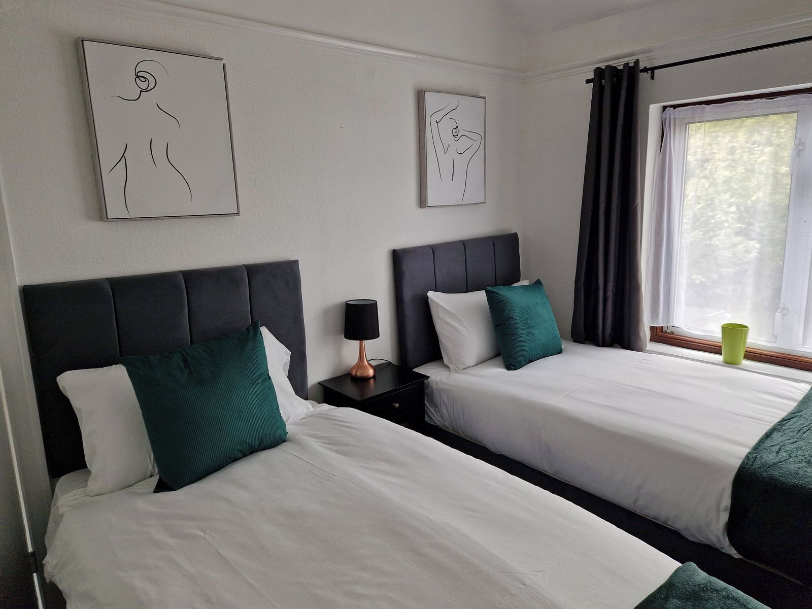 Habitació d'hotel amb dos llits, una tauleta de nit amb una làmpada i obra d'art a les parets.