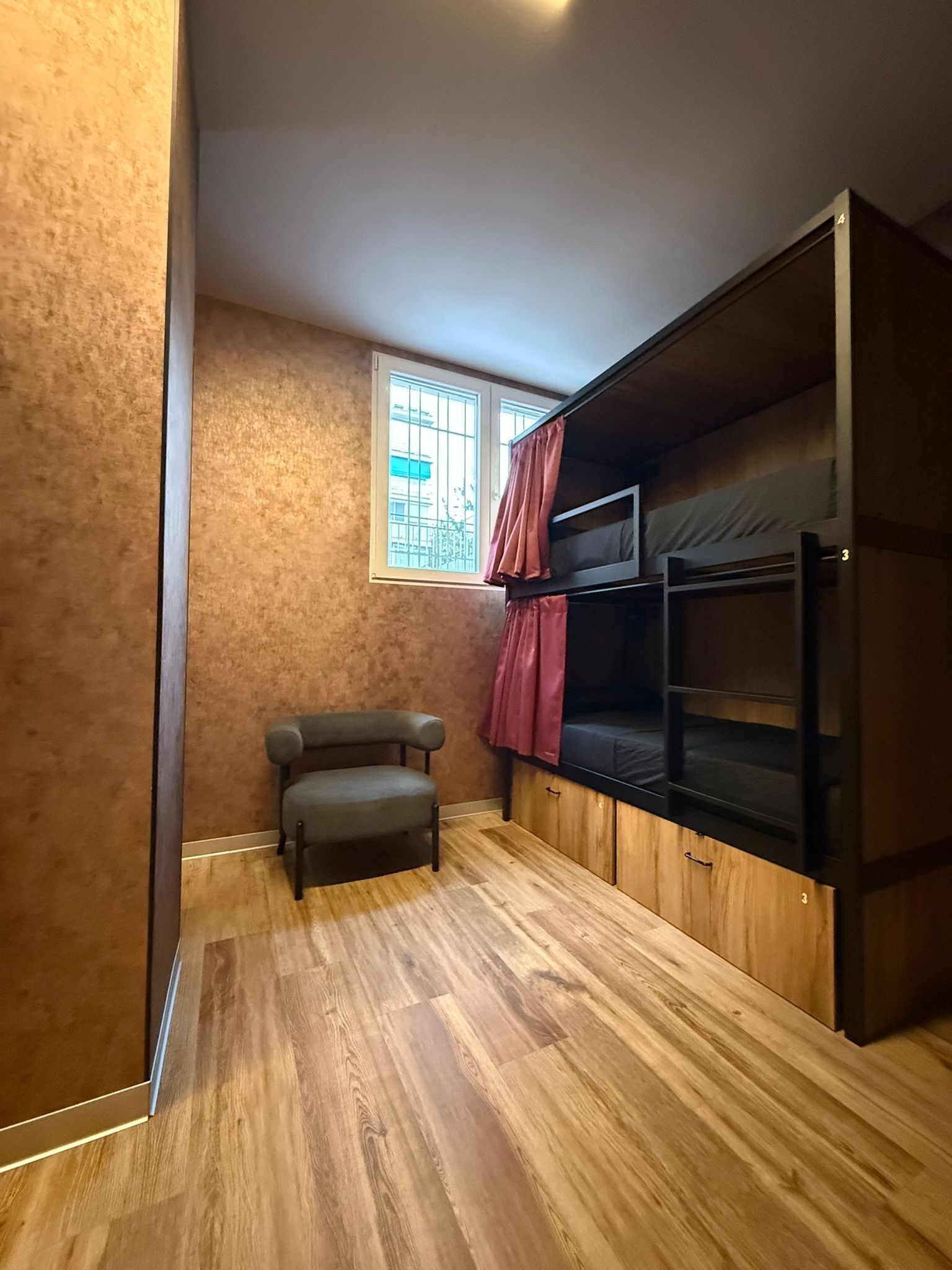 A compact room with a bunk bed, a small sofa, and a window with curtains.