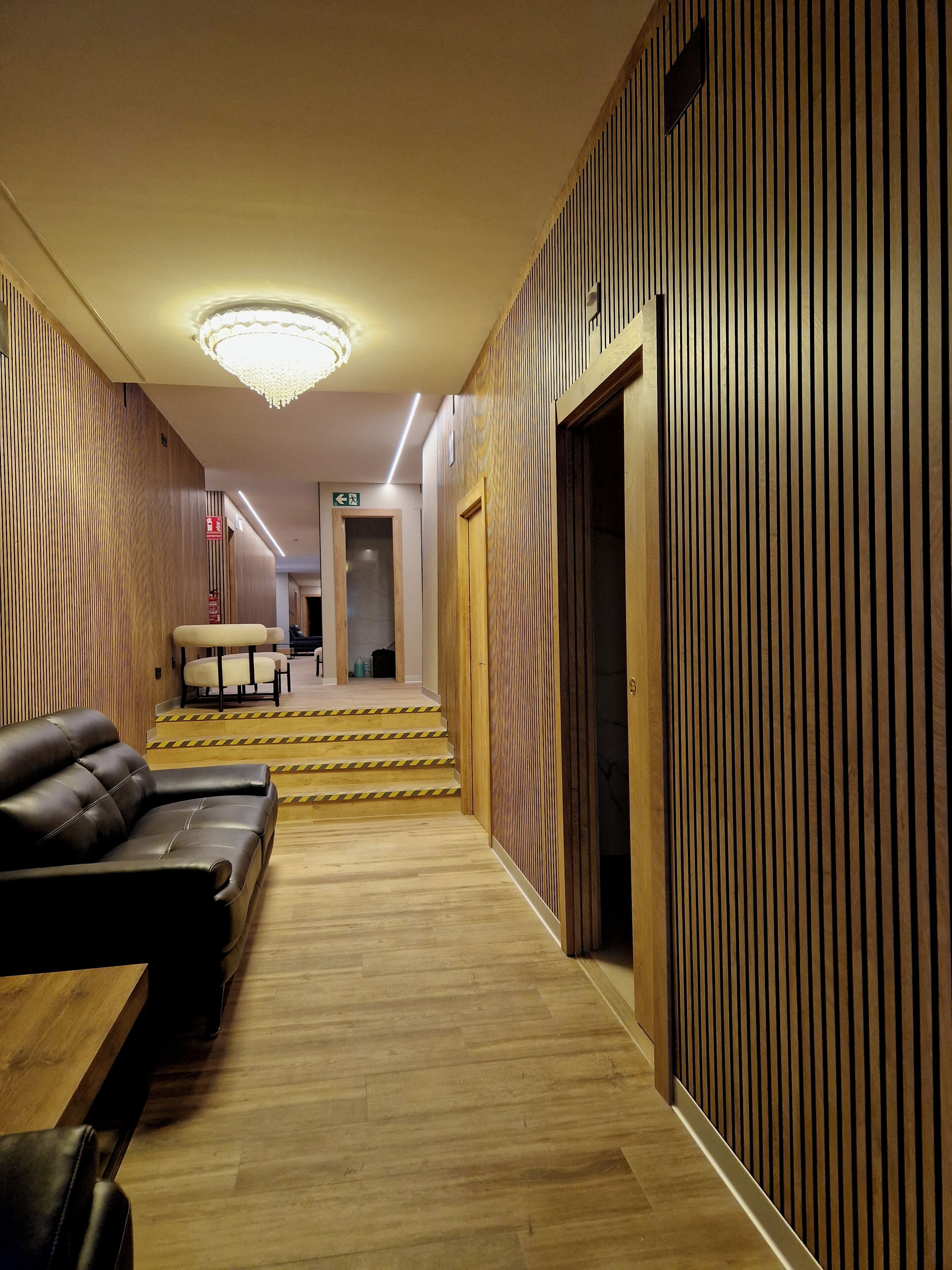 Un moderno vestíbulo de hotel con un panel de pared de madera, un sofá de cuero negro, una escalera de madera y una araña.