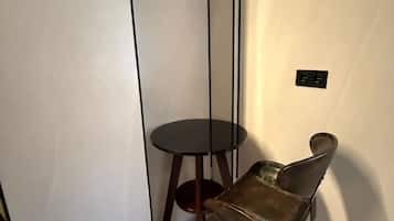Un rincón de una habitación con piso de madera, una mesa redonda pequeña y una silla de base metálica.