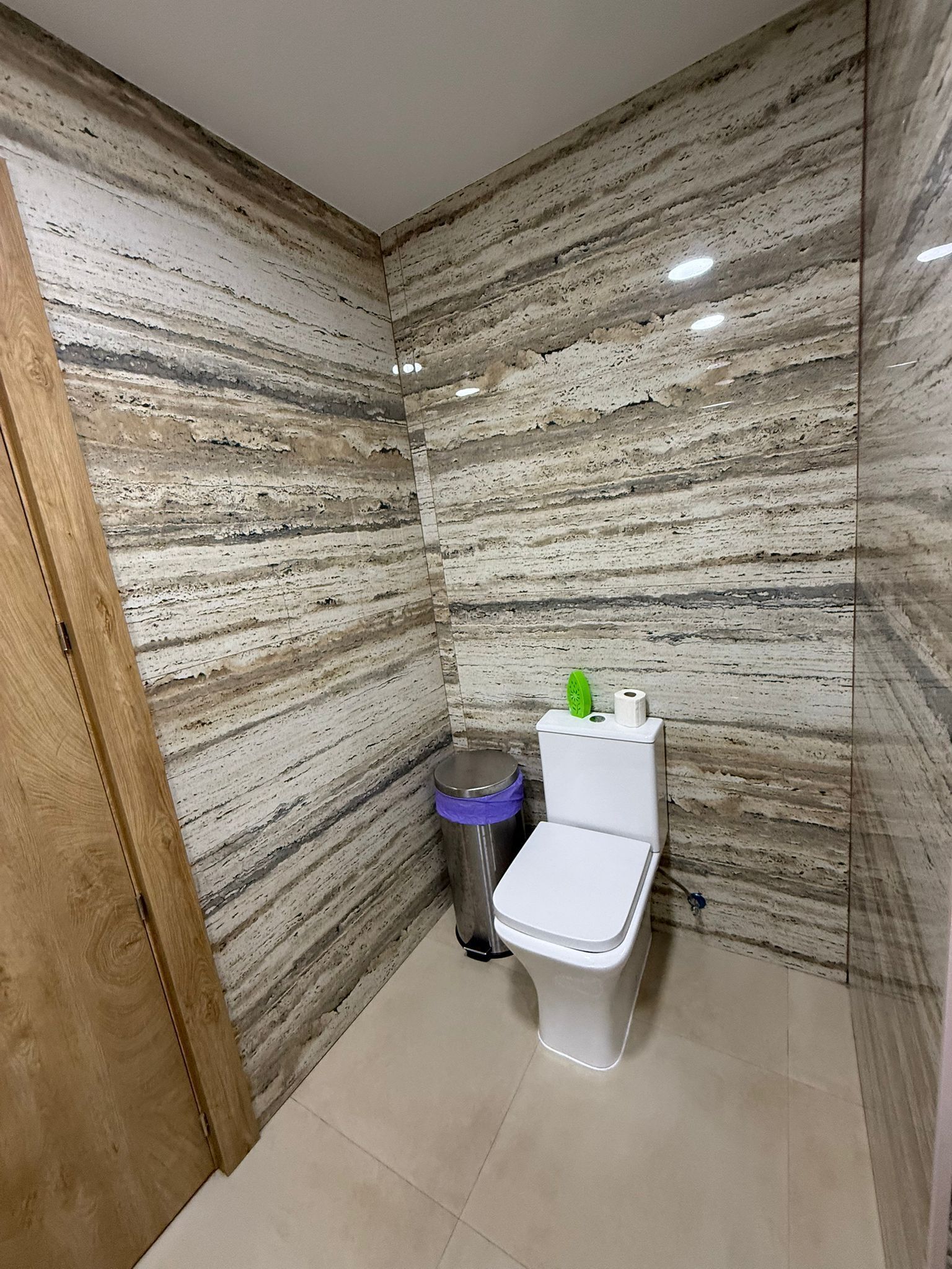 A small bathroom with a toilet, a trash bin, and a wooden door.