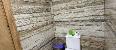 A small bathroom with a toilet, a trash bin, and a wooden door.