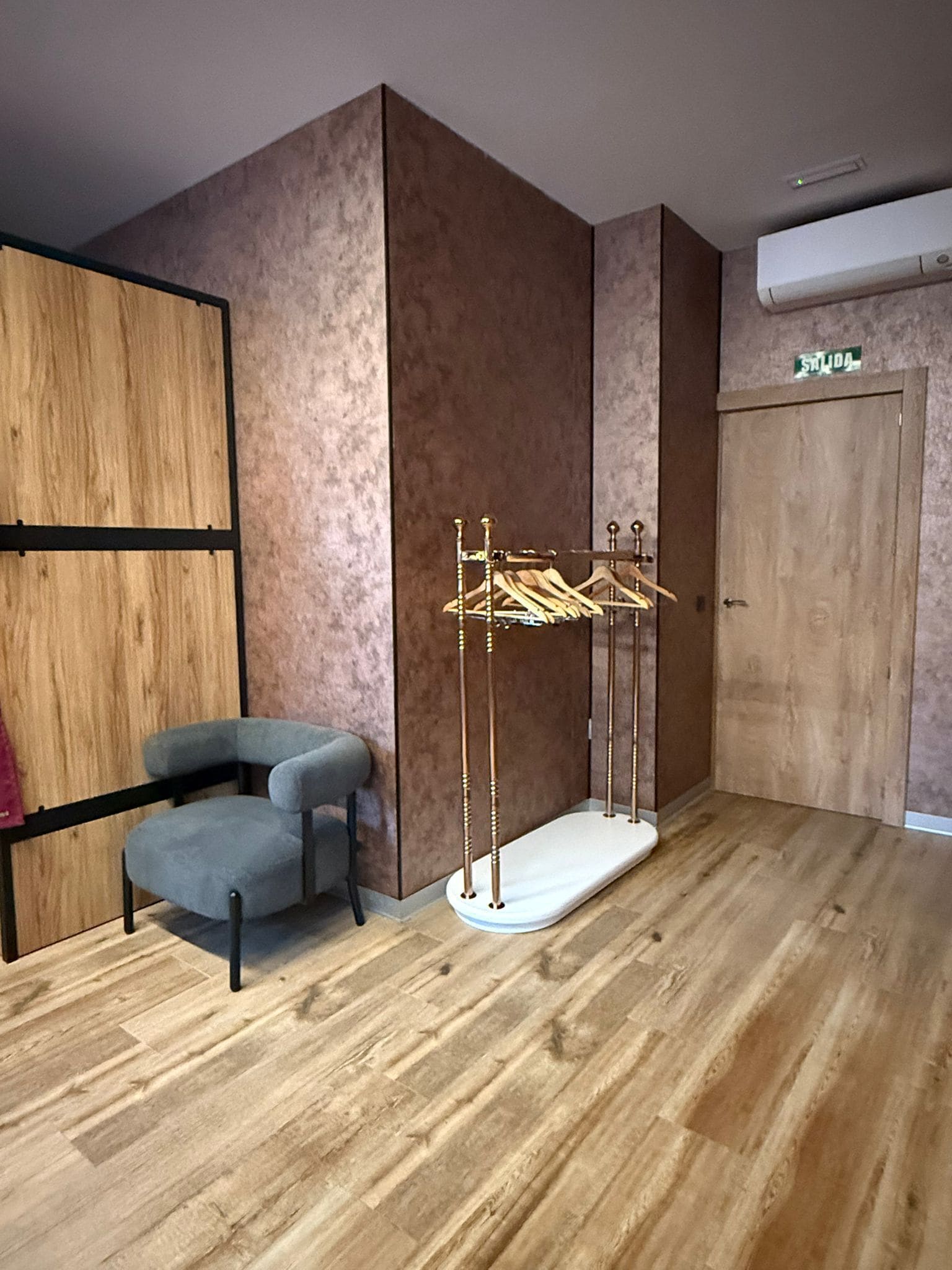 Una stanza con pavimento in legno, una sedia grigia, un armadio in legno e uno stendibiancheria.