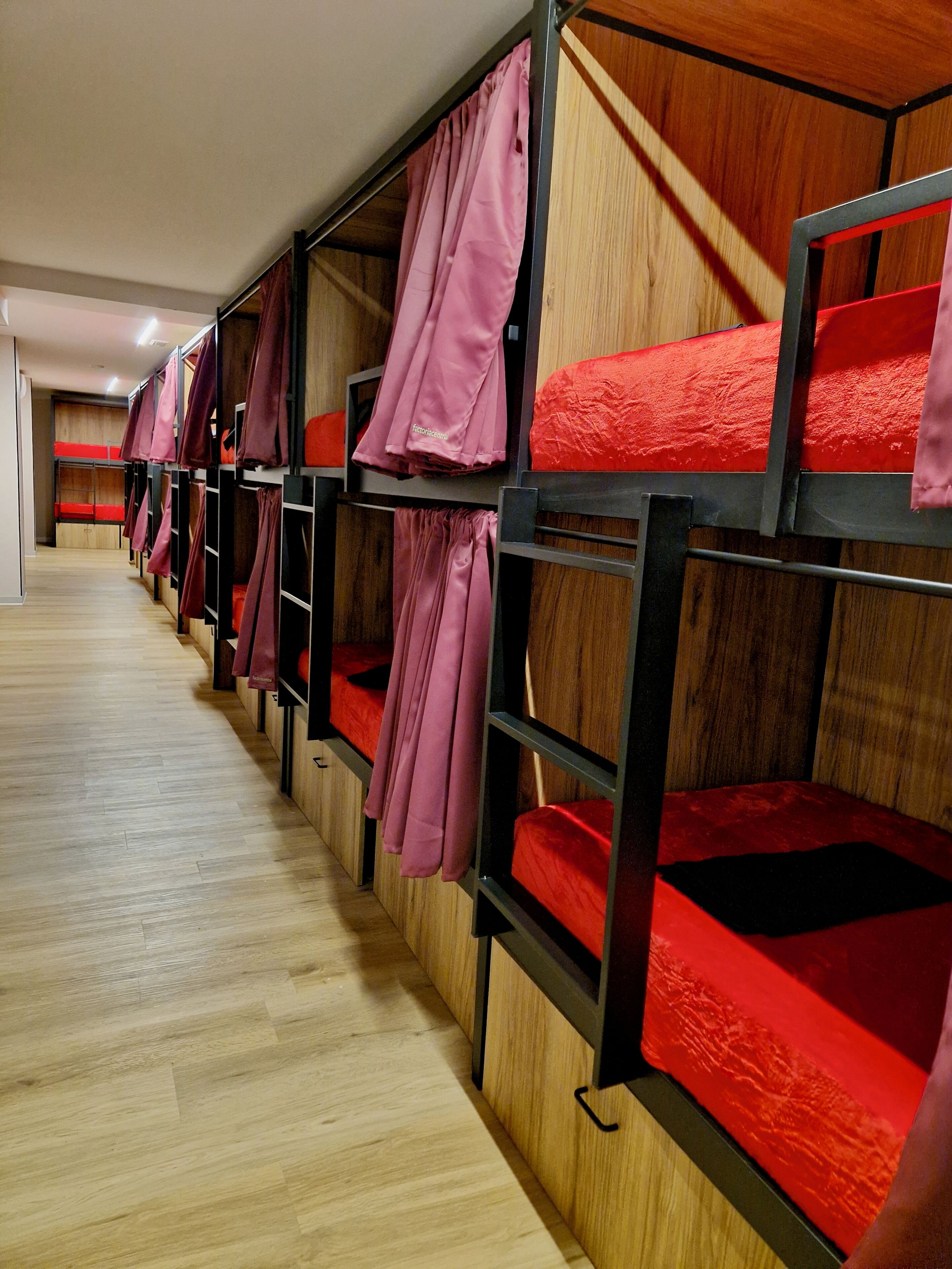 A row of bunk beds with red mattresses and pink curtains, wooden flooring, and a wooden wall.