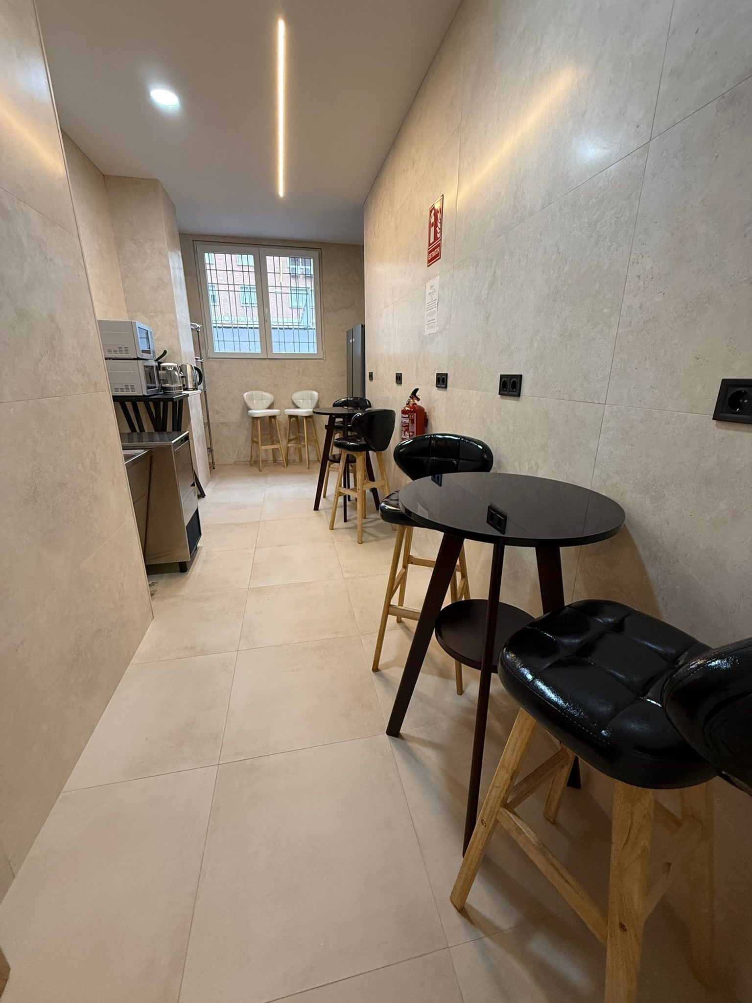 A modern kitchen with a microwave, coffee maker, and a fire extinguisher. There are four stools and a table with chairs.