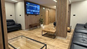 A modern lounge area with a large flat-screen TV, wooden paneling, black leather sofas, and a glass coffee table. - Velvet Hostel Business (Madrid)