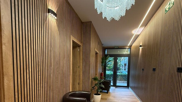 A modern hallway with wooden paneling, a wooden bench, a chandelier, and a view of the outdoors. - Velvet Hostel Business (Madrid)