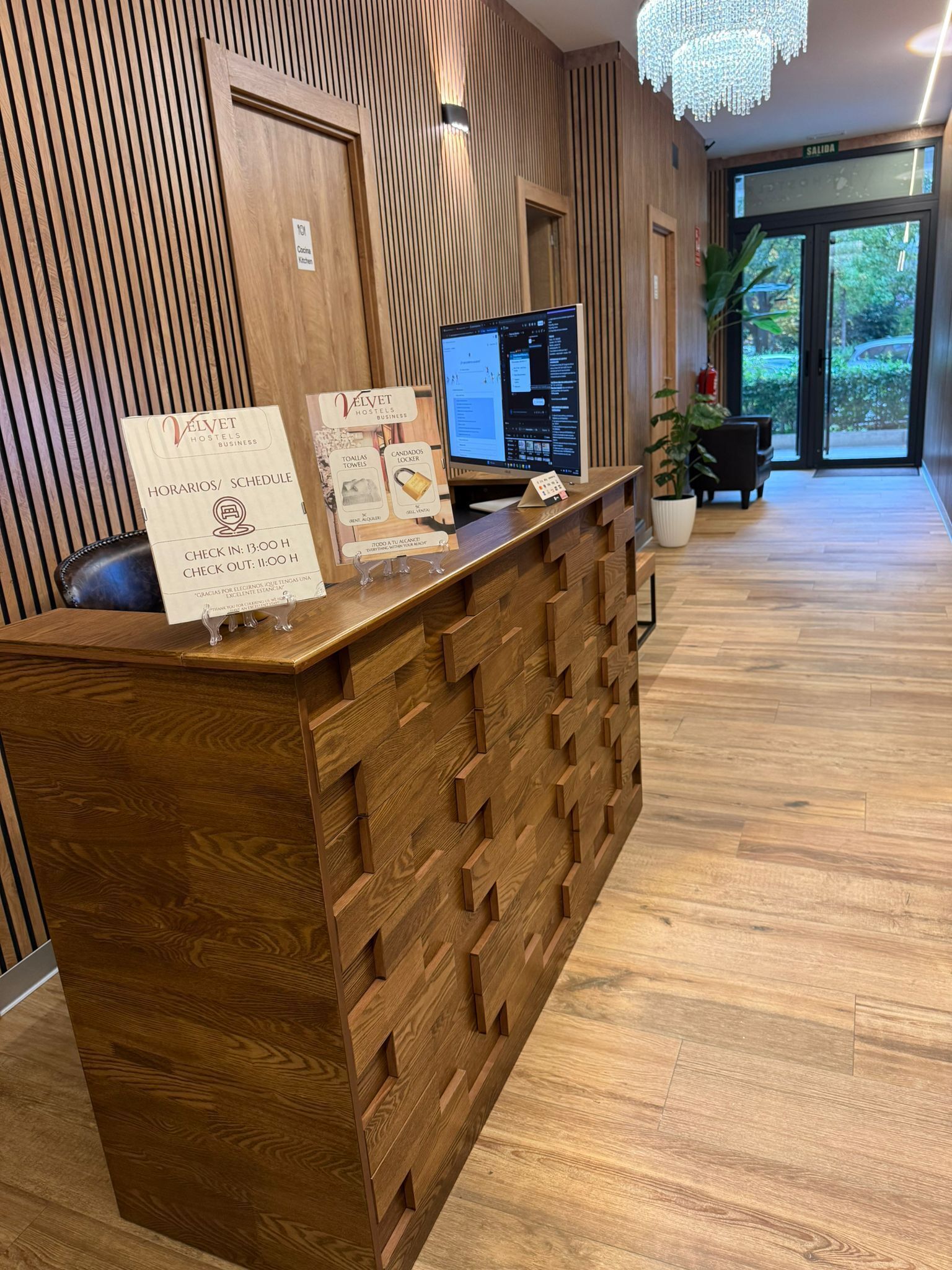 A reception desk with a wooden design, a computer monitor, and a signboard displaying check-in and check-out times.
