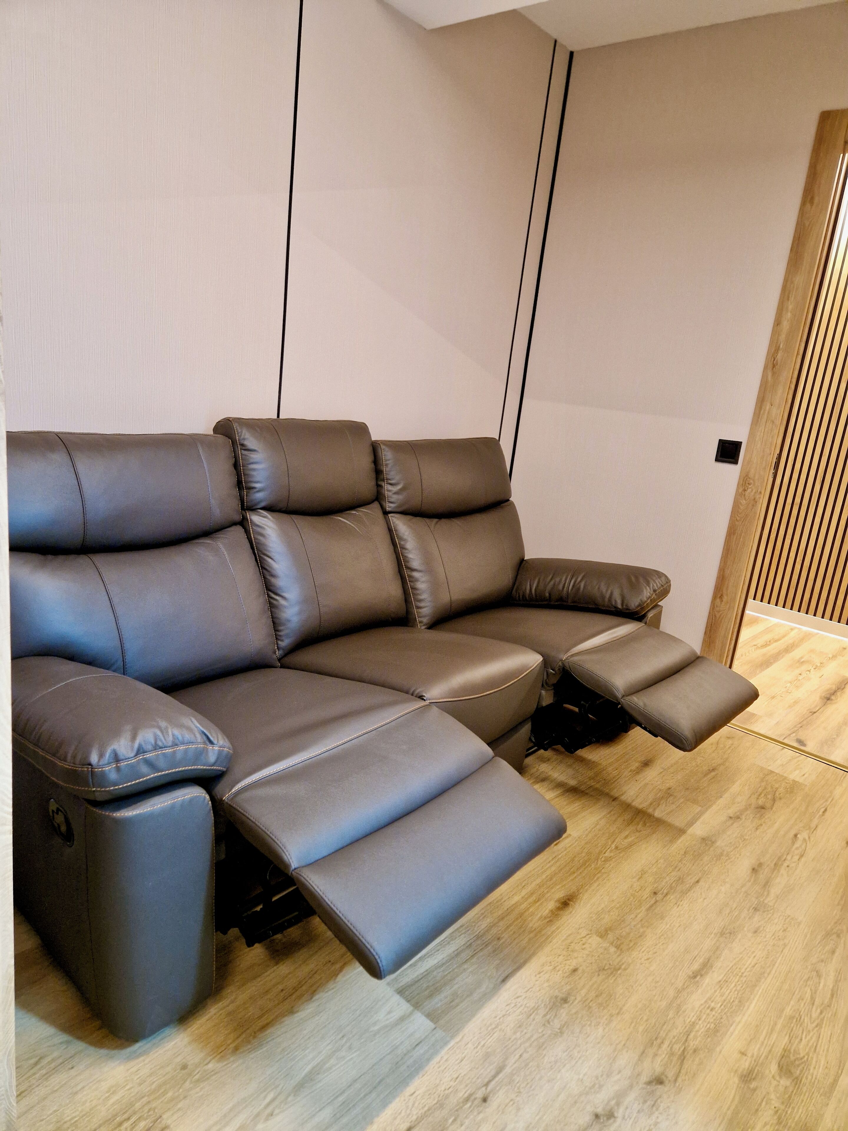 A sectional sofa with reclining and adjustable features, positioned in a room with wooden flooring and a plain wall.