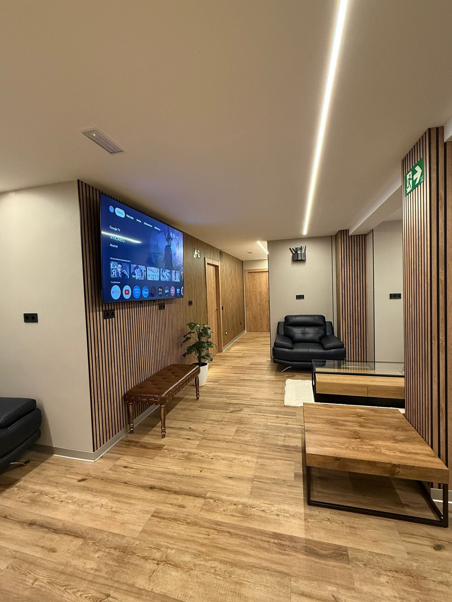 Un espace d’attente moderne doté d’un grand écran numérique diffusant une chaîne de télévision, d’un banc, d’un canapé et d’un comptoir d’accueil.