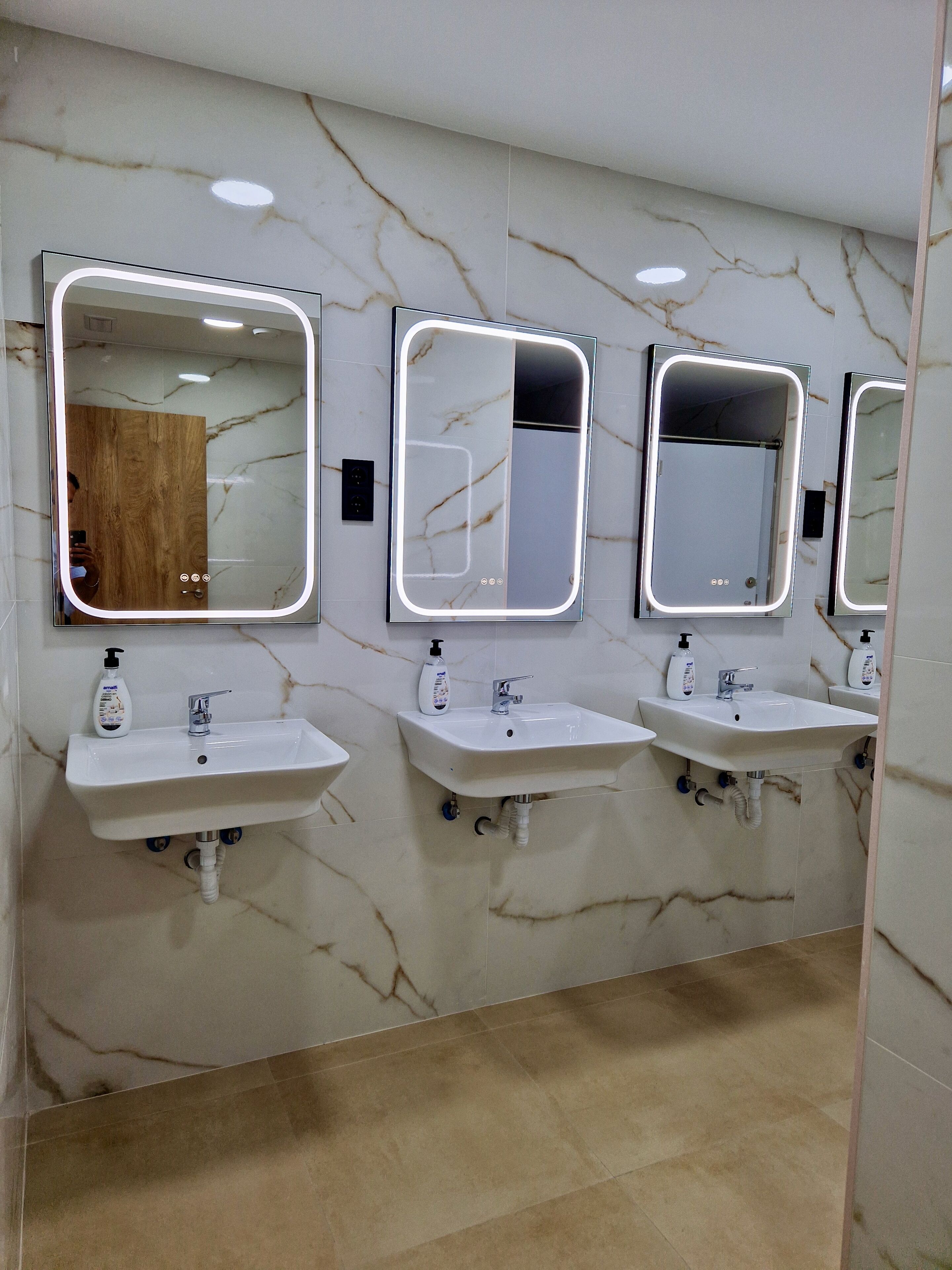 A bathroom with three sinks and mirrors, marble walls, and a wooden door.