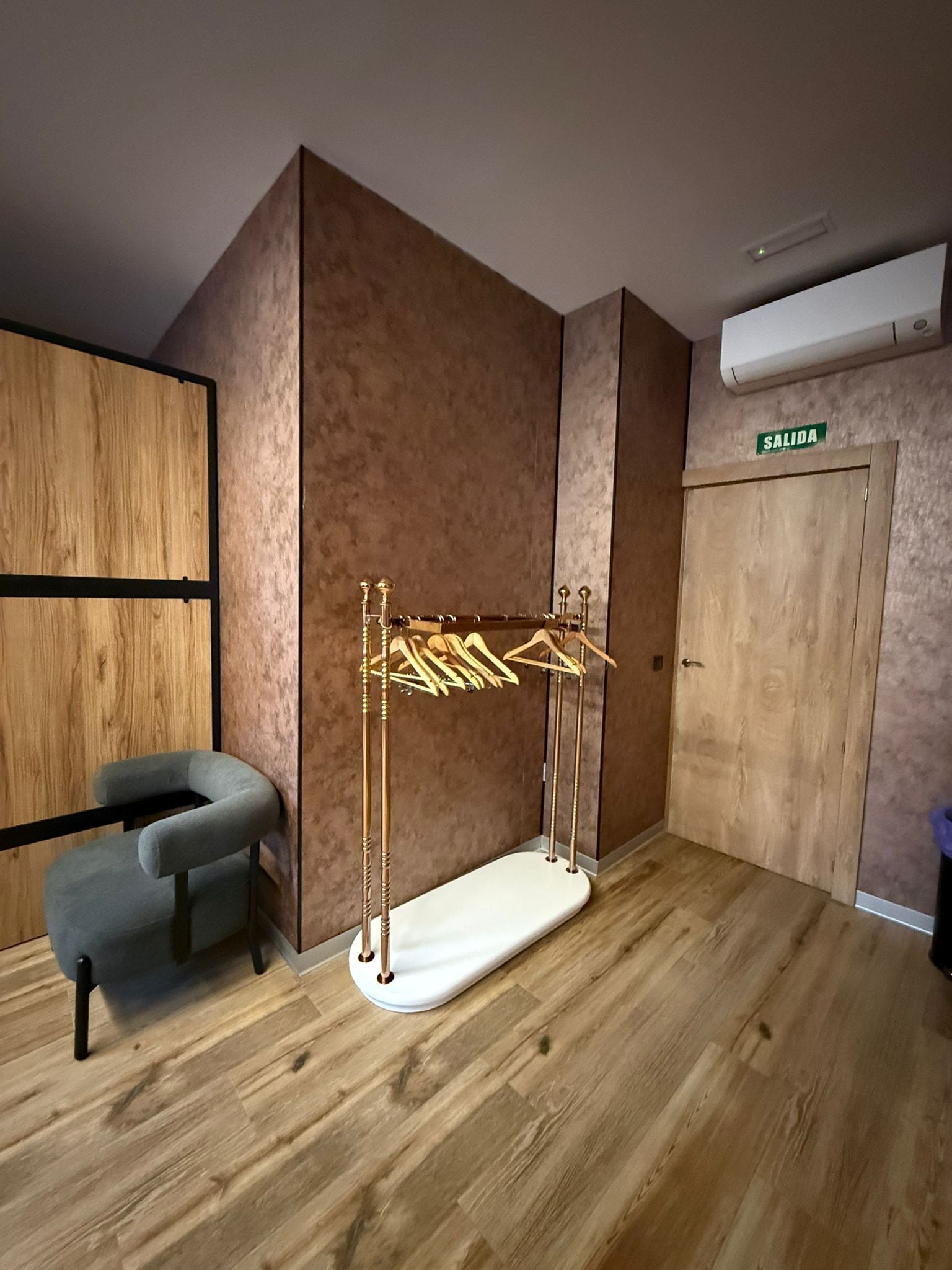 Een kamer met een houten vloer, een grijze stoel, een houten garderobe en een kledingrek.