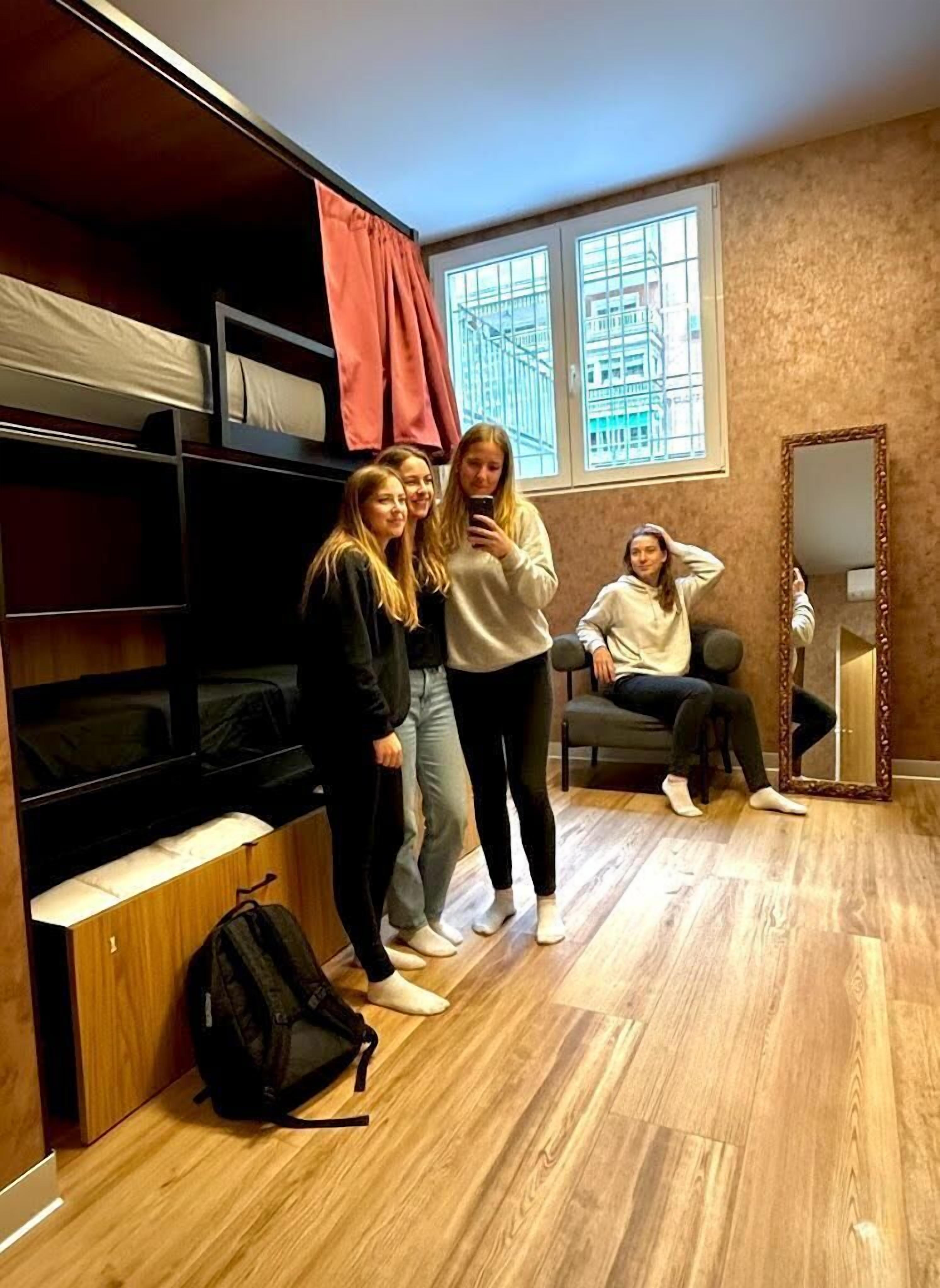 Una habitación con literas, un espejo y una ventana con vistas a edificios.
