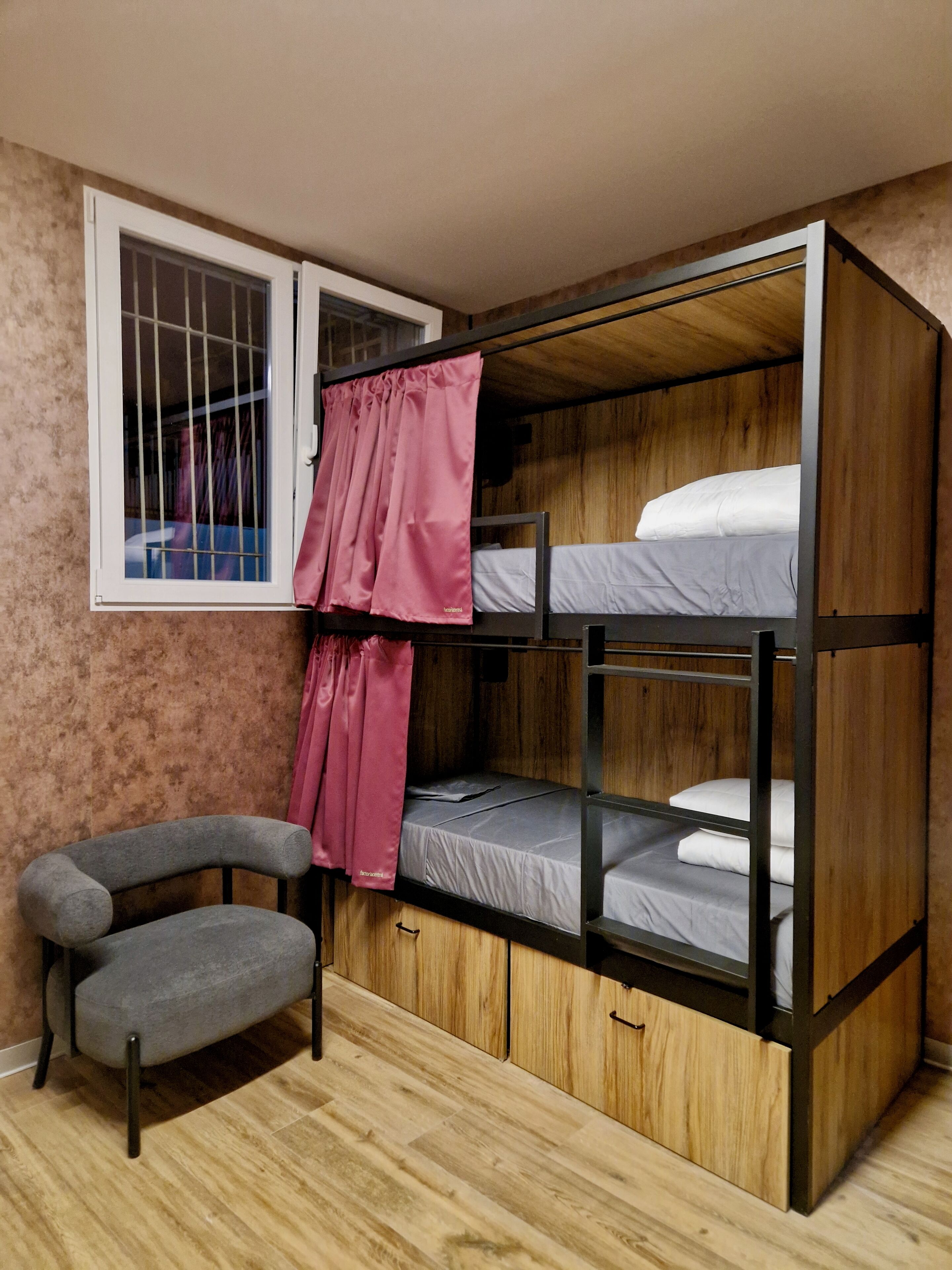 Habitación pequeña con literas, una silla y ventana con cortinas.
