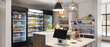 Un espacio comercial moderno con un expositor refrigerado, una caja registradora y estantes llenos de productos.