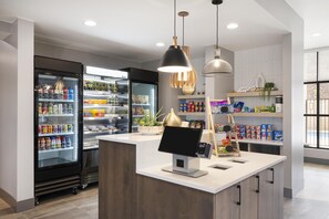A modern retail space with a refrigerated display, a checkout counter, and shelves stocked with products. - @HOME by Best Western St. George (St. George)