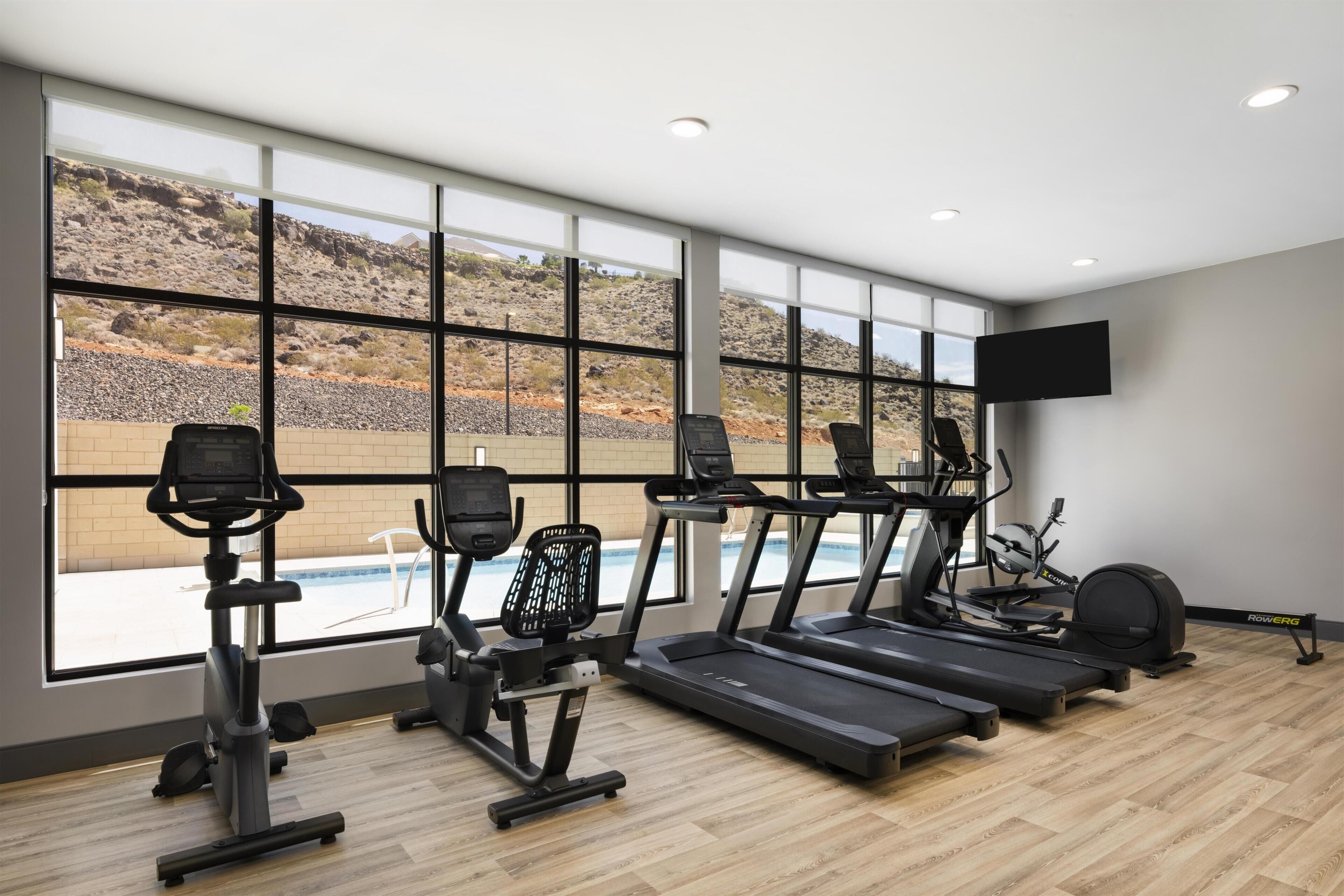 A gym with treadmills, elliptical machines, and a pool view.