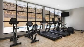 A gym with treadmills, elliptical machines, and a pool view.