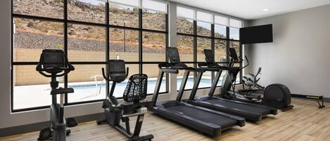 A gym with treadmills, elliptical machines, and a pool view.