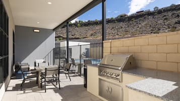 Un patio exterior con una parrilla, zona de estar y vistas a una piscina y terreno rocoso.