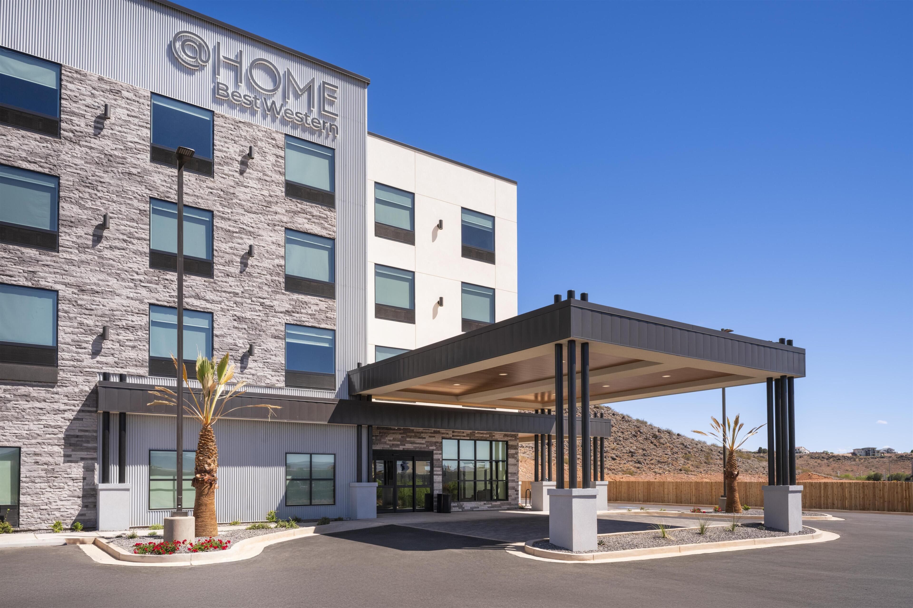 A modern hotel with a stone facade, a covered entrance, and a landscaped entrance area.