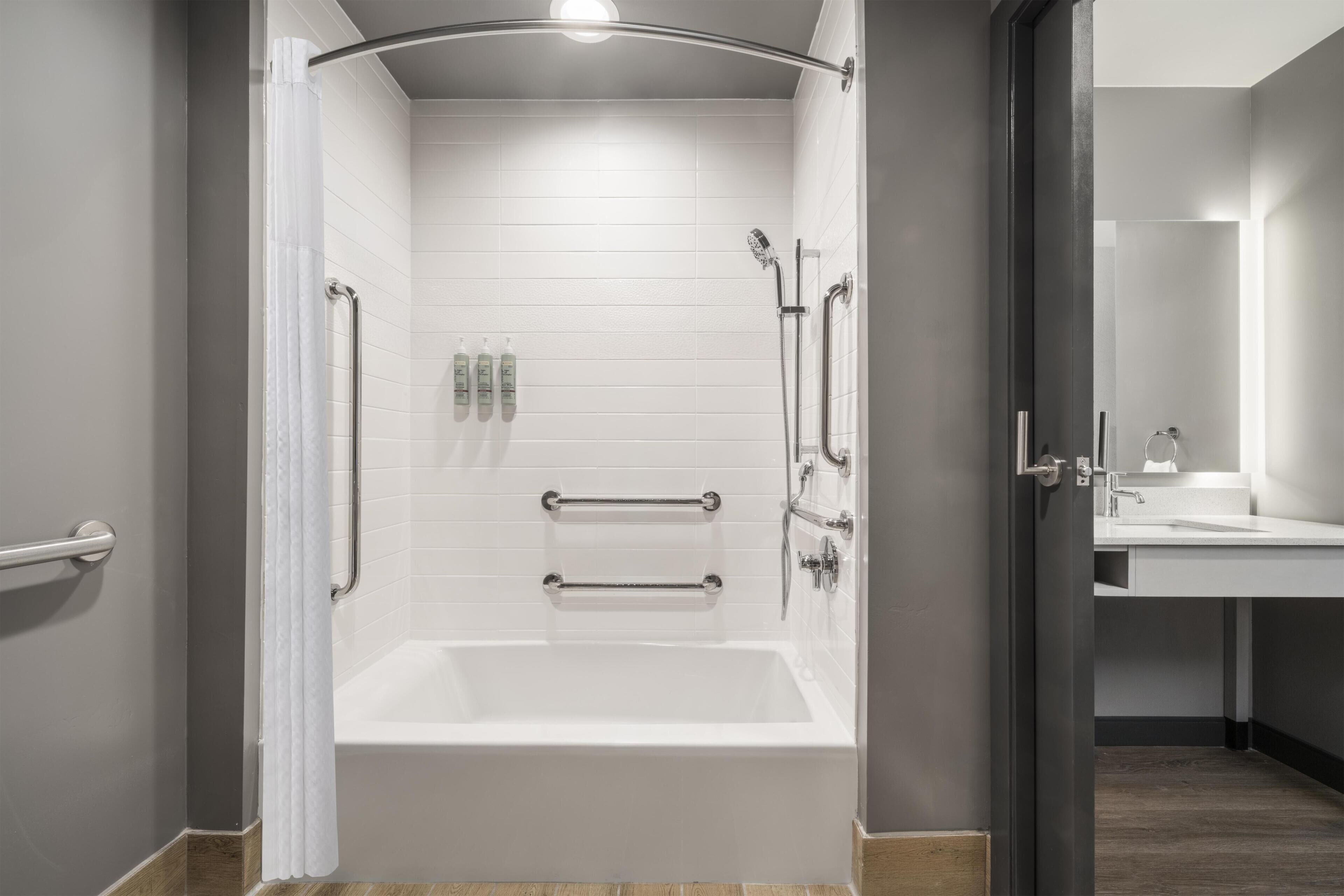 A modern bathroom with a walk-in shower, grab bars, and a visible toilet paper dispenser.