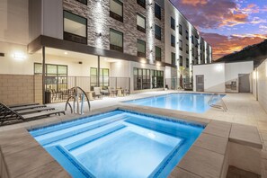 A swimming pool with a modern building in the background, a covered seating area, and a clear sky. - @HOME by Best Western St. George (St. George)