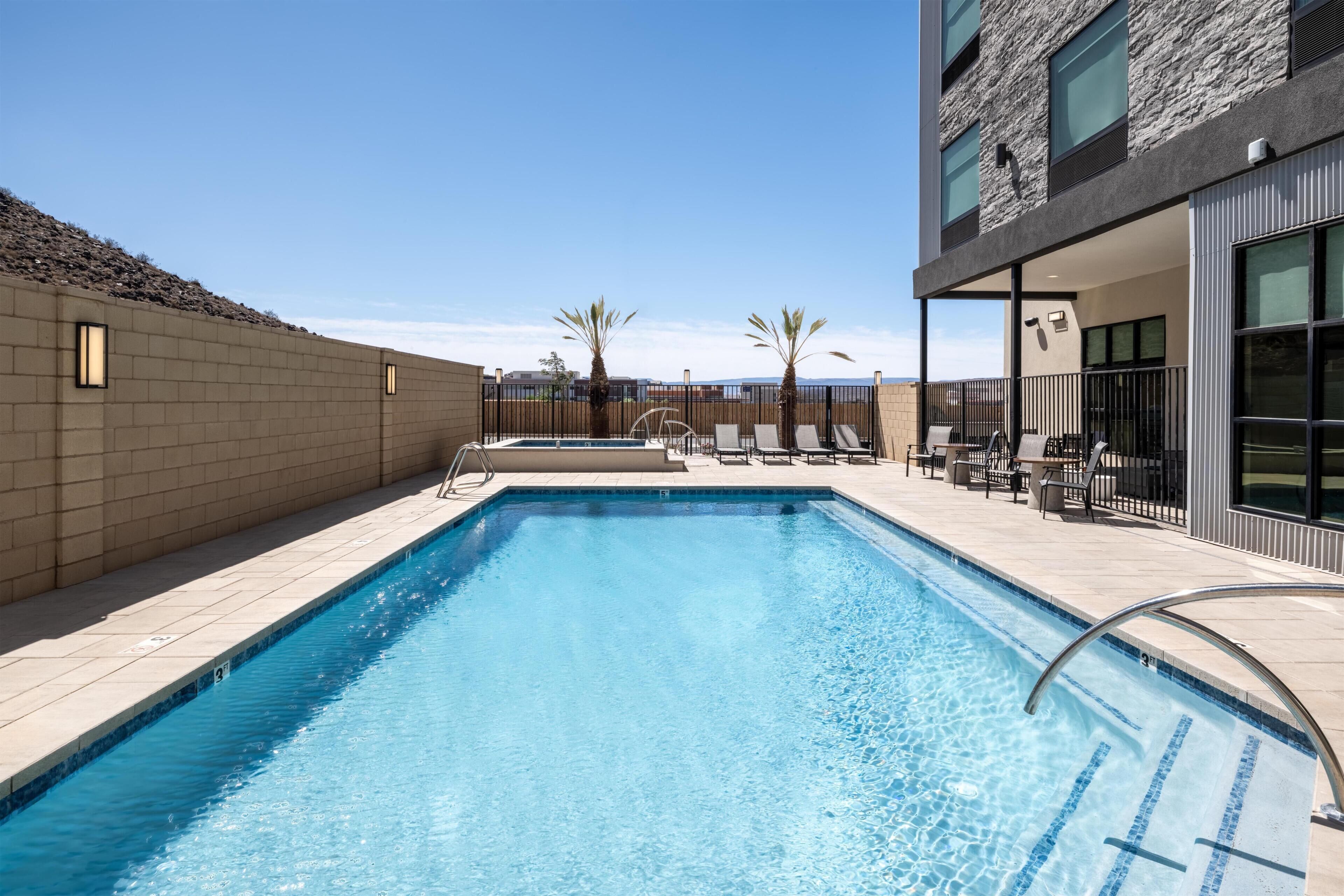 A rectangular swimming pool with a tiled edge, surrounded by a low brick wall and a wooden fence.