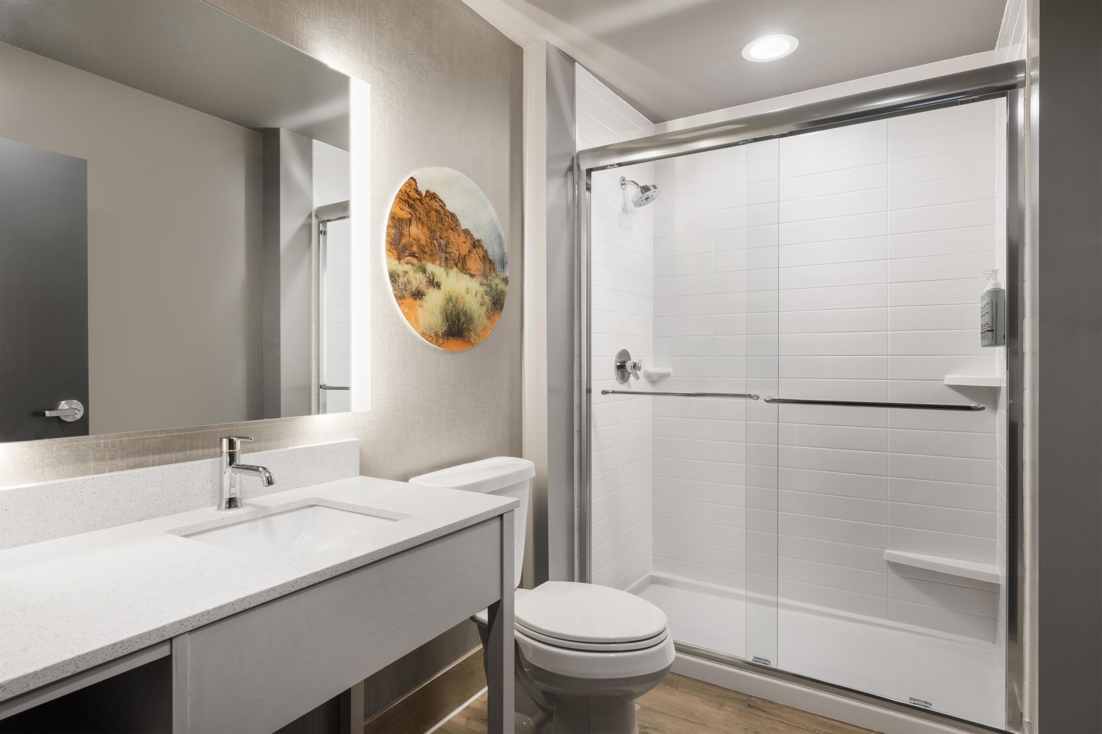 Et badeværelse med hvid vask, spejl, toilet og brusekabine med glasvægge.