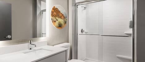 A bathroom with a white sink, mirror, toilet, and glass-enclosed shower.