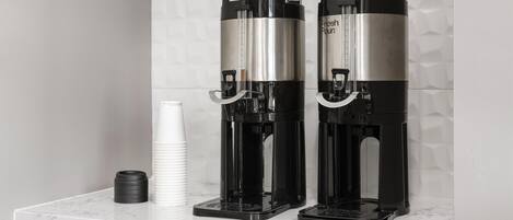 Deux distributeurs de café sont posés sur un comptoir en marbre, avec un mur recouvert de carreaux blancs en arrière-plan.