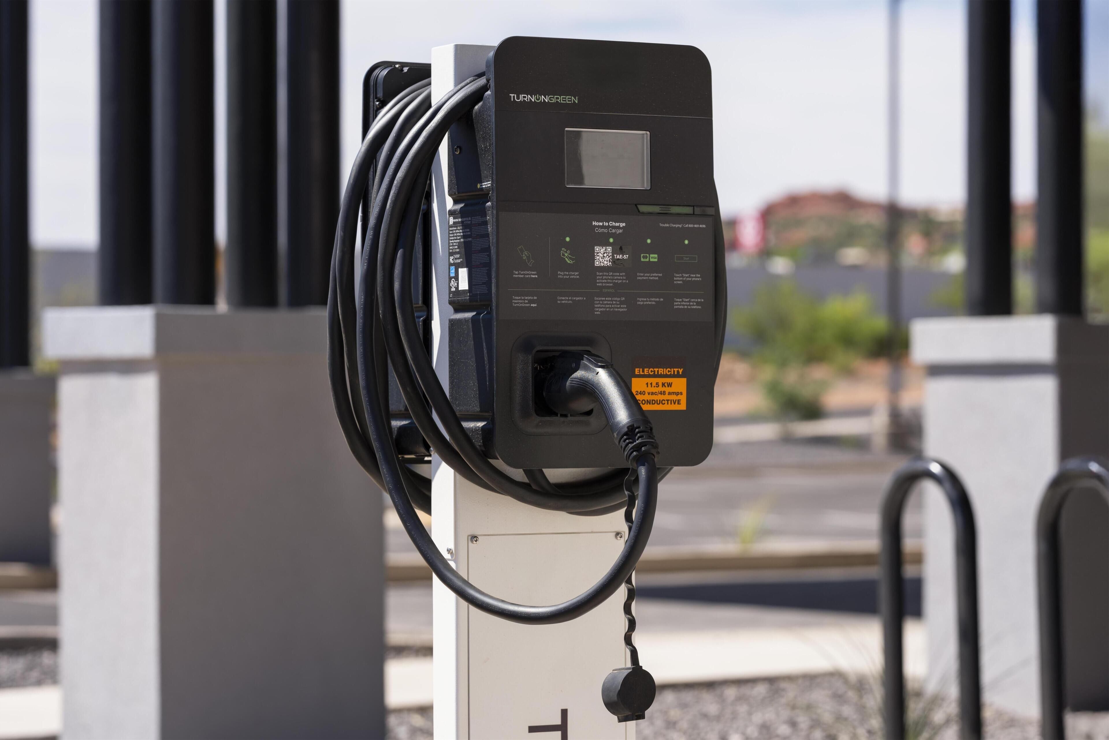 Une borne de recharge dotée d’un écran numérique, d’un code QR et d’un câble relié à un véhicule.