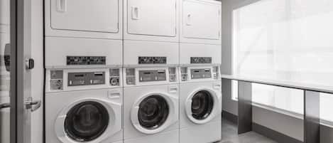 A laundry facility with multiple washing machines and dryers, a tiled floor, and a window with a view.