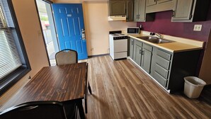 A compact kitchen with a blue door, a microwave, a stove, and wooden flooring. - Travelers Inn and Suites (Paducah)