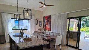 Una cocina moderna con una isla central, comedor con sillas y un ventanal grande.