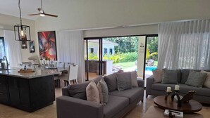 Amplia sala de estar con un sofá gris, una mesa de centro y una zona de cocina con mesa de comedor.