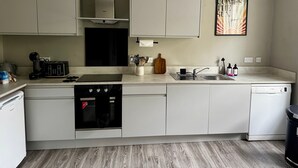 Et moderne køkken med hvide skabe, en Bosch opvaskemaskine, kaffemaskine og brødrister.