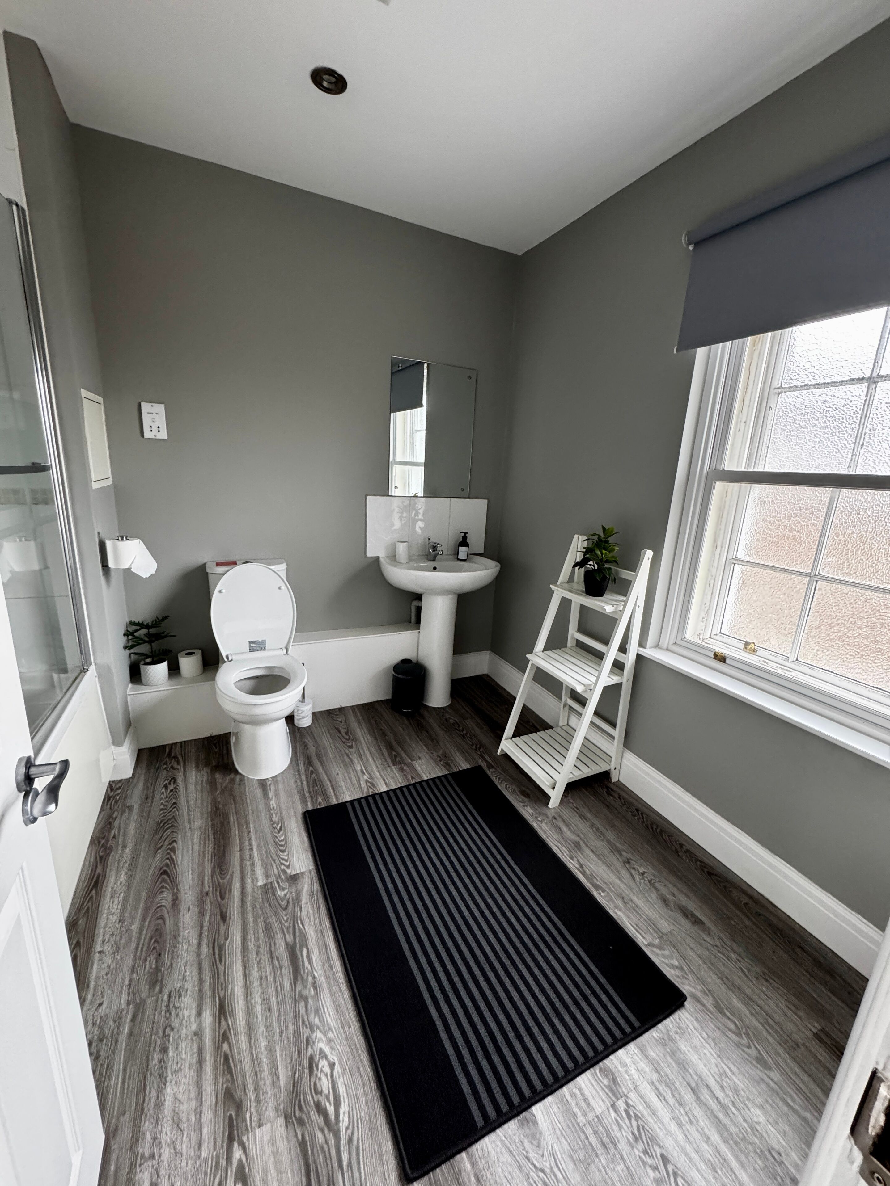 A bathroom with a toilet, sink, mirror, and a window.
